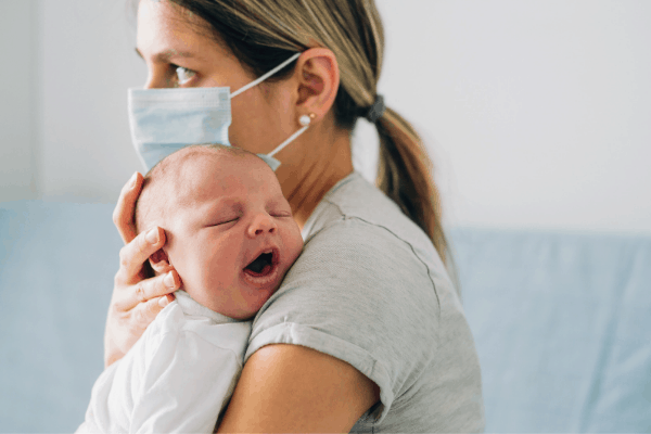 new mom wearing a mask while holding her newborn