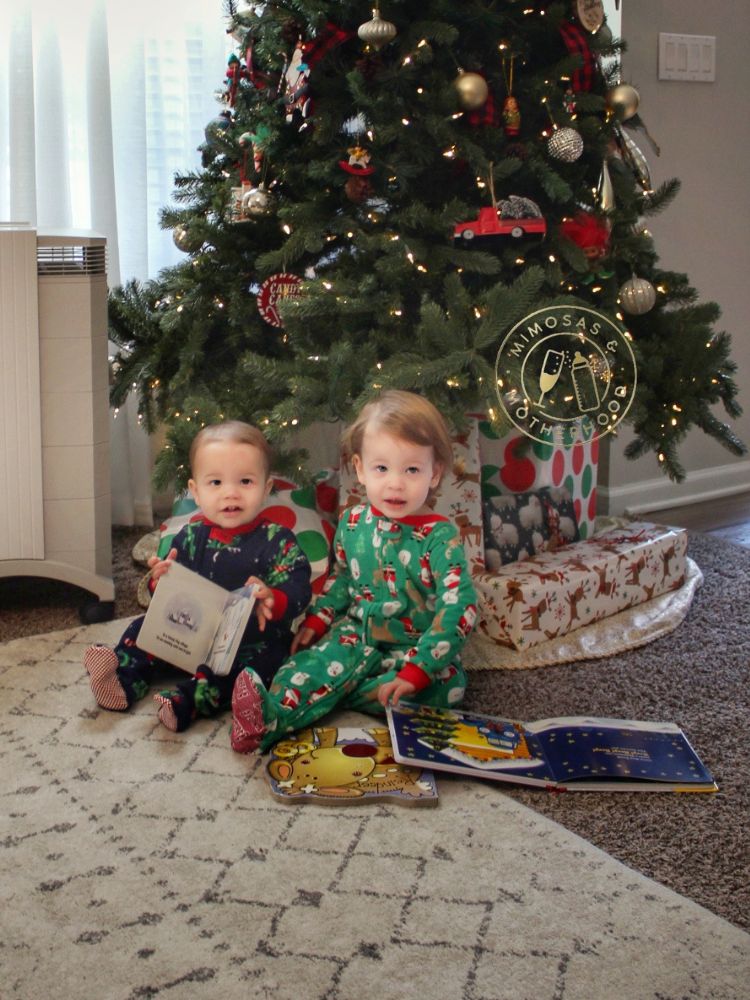 Image shows 2 children in front of the Christmas tree with Christmas books.