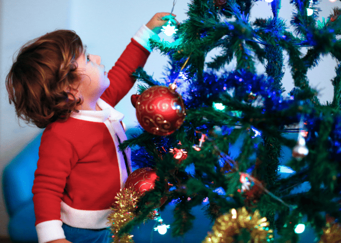 image shows a child hanging ornaments on a tree