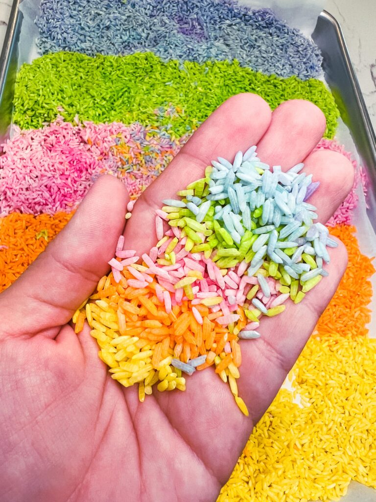 hand holding rainbow rice that's been dyed with food coloring for sensory bin