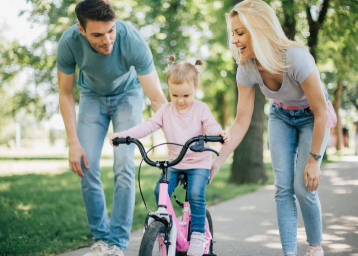 image shows a family teaching a child to ride a bike