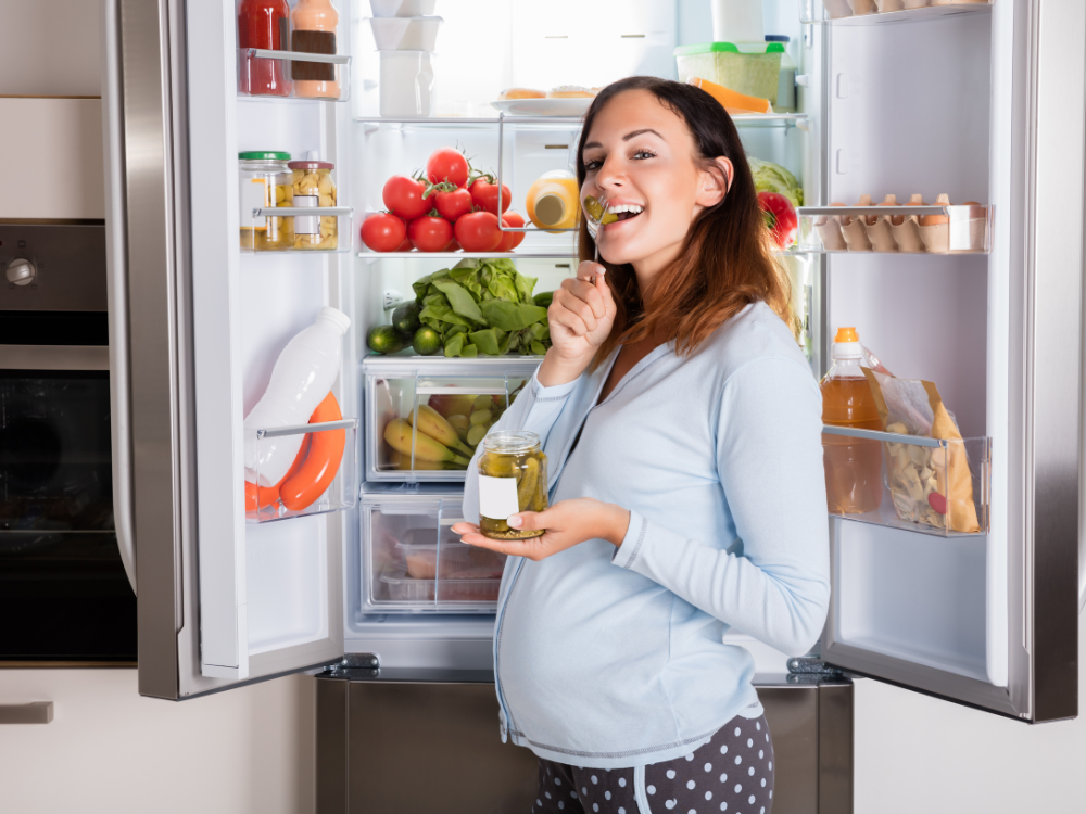 pregnant woman eating in front of a refrigerator