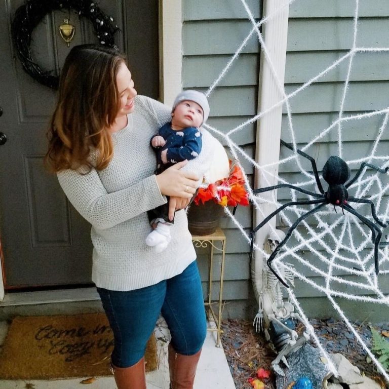 woman holding a baby in front of a halloween spiderweb