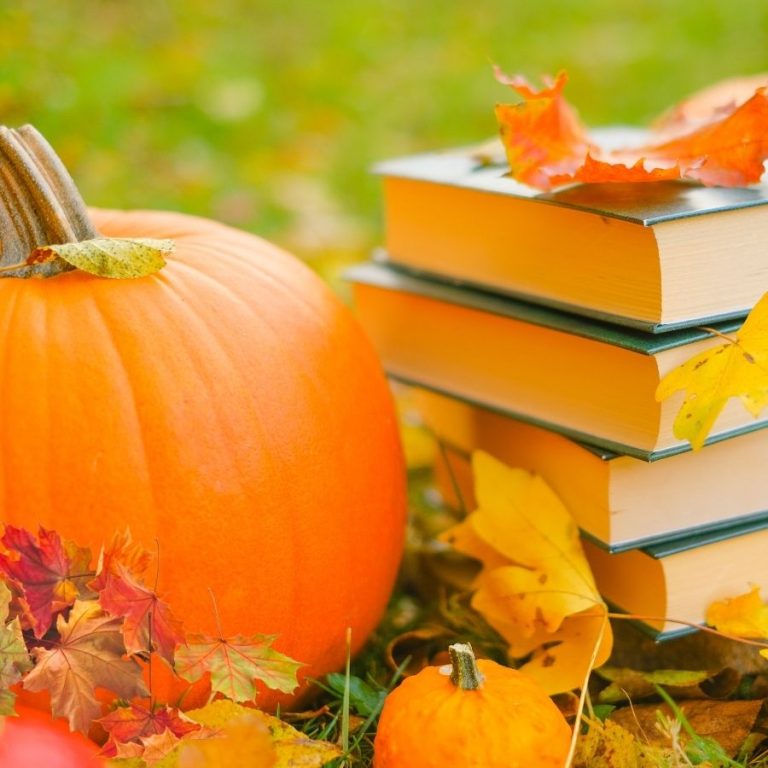 image shows a stack of books with a pumpkin and fall leaves