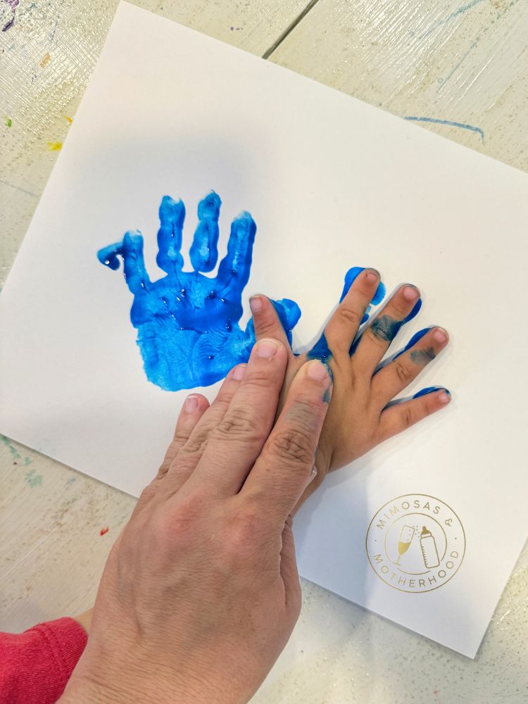 image shows a child's hands being pressed into paper to make Hanukkah handprint art