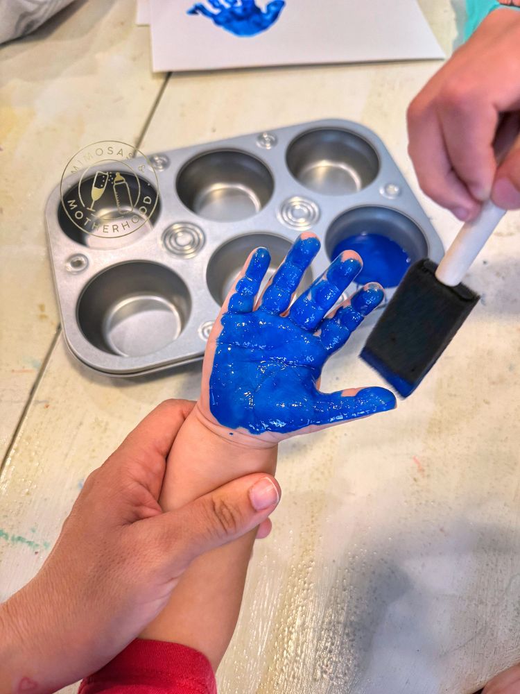 image shows a preschooler's hand being painted with blue paint