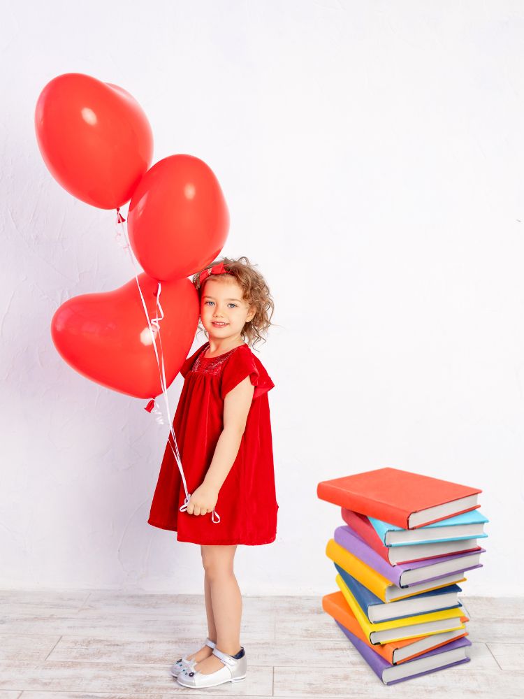 child holding heart balloons next to a stack of books